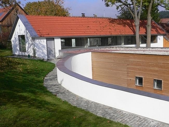 Passivhaus in Essenbach: Die ehemalige Hofstelle liegt an einem Hang und wird teilweise von einer im Bogen verlaufenden Mauer umfasst. Foto: Leipfinger-Bader